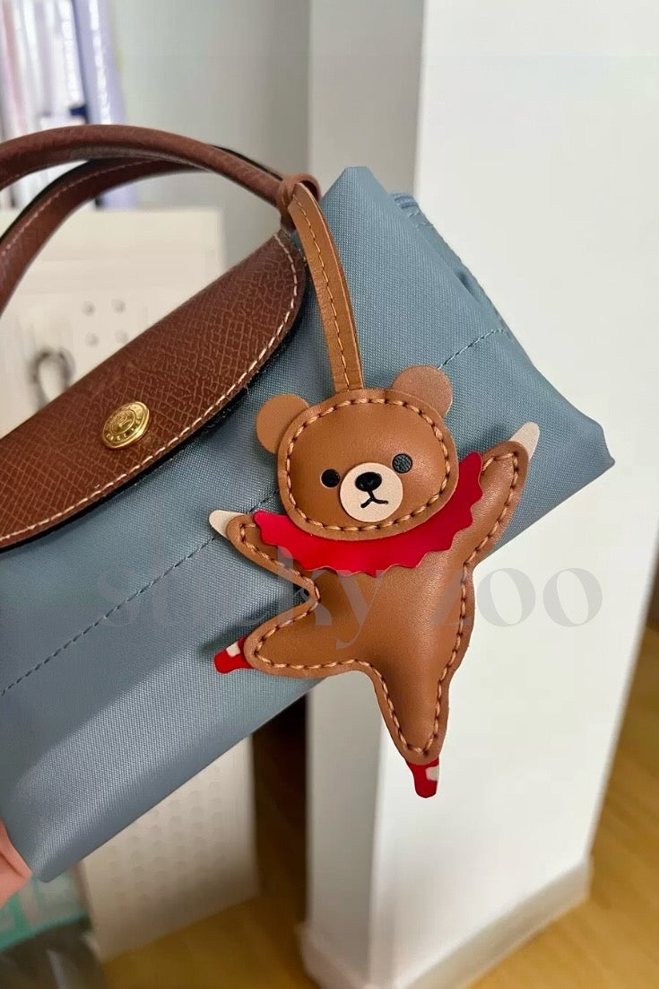Both editions of the ballet bear charm — leather strap loop for bags, or 18K gold-plated keychain clip.