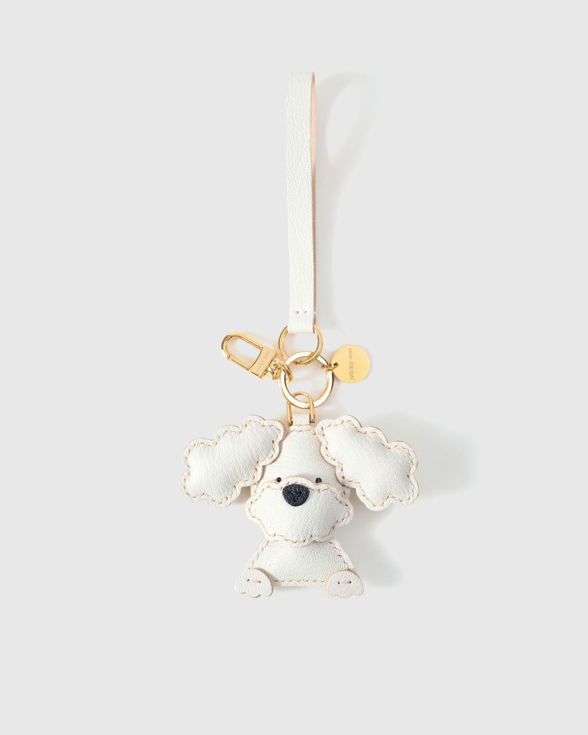 Close-up of handmade Poodle leather bag charm — hand-stitched visible edges on French Alran goatskin, 18K gold-plated cube hardware. STICKYZOO.