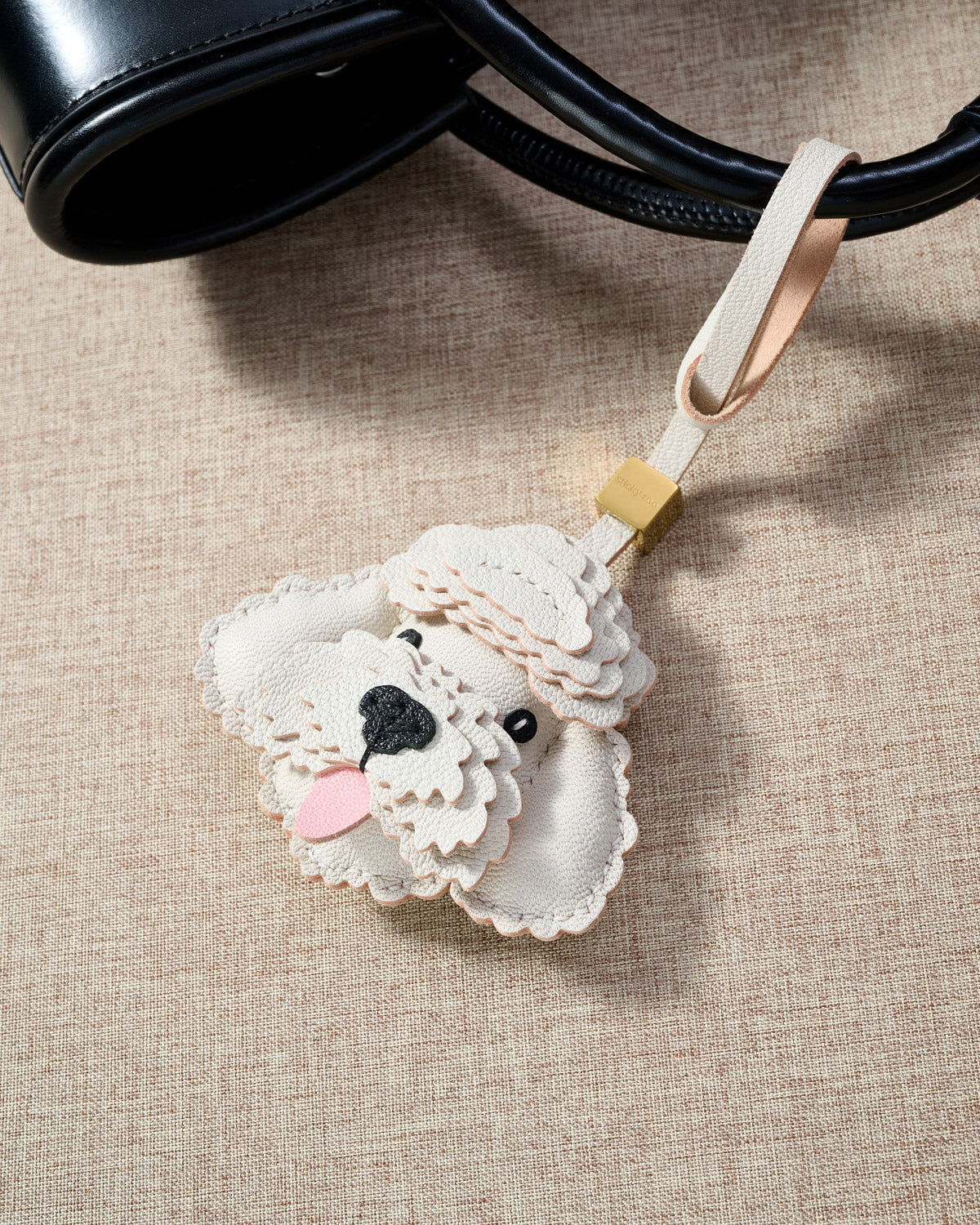 Close-up of handmade Poodle leather bag charm — hand-stitched visible edges on French Alran goatskin, 18K gold-plated cube hardware. STICKYZOO.