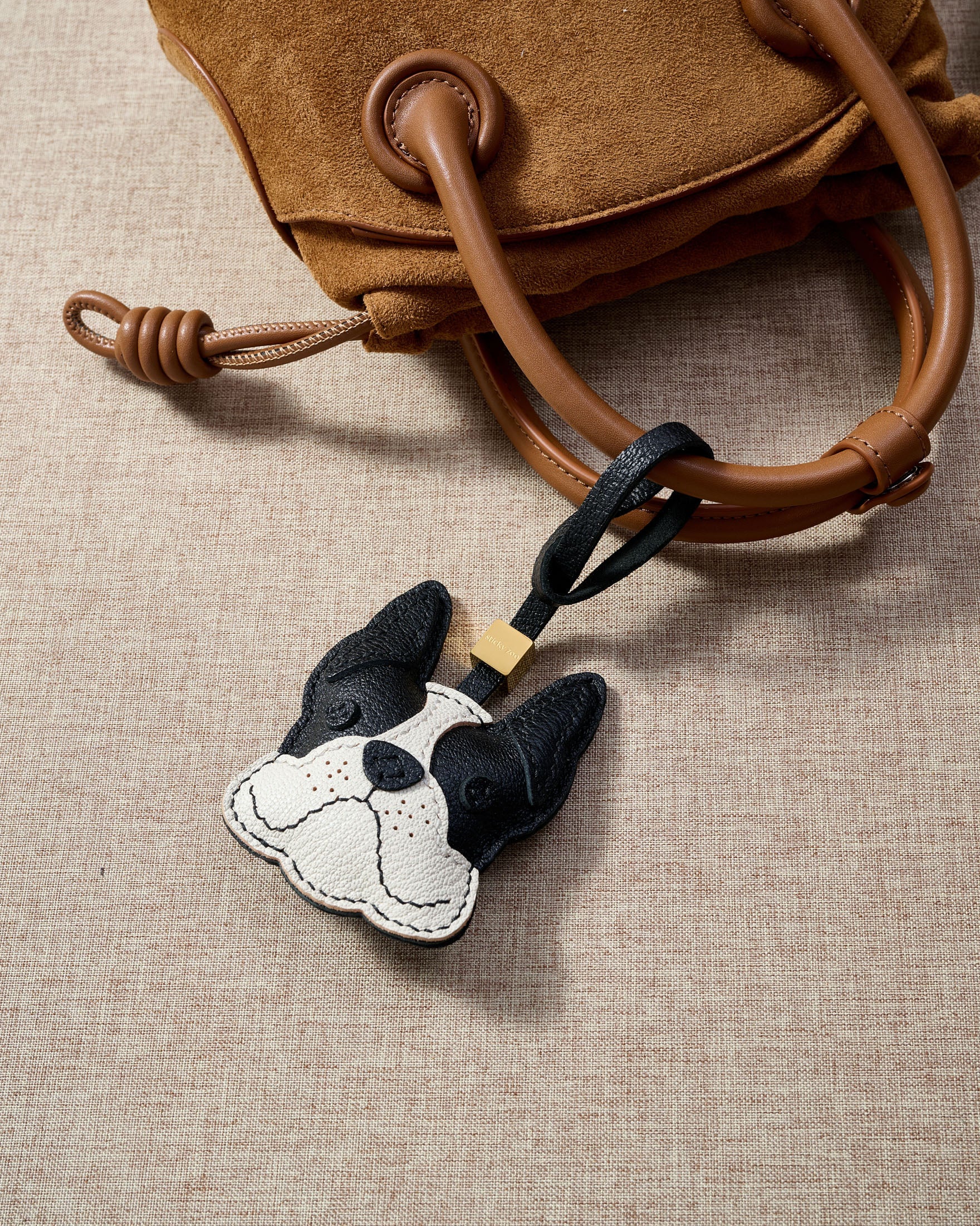 Close-up of handmade French Bulldog leather bag charm — hand-stitched visible edges on French Alran goatskin, 18K gold-plated cube hardware. STICKYZOO.