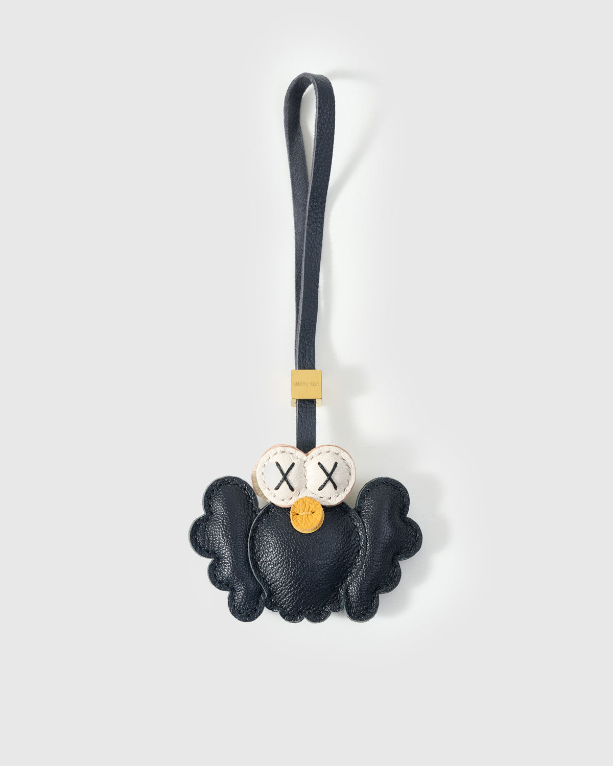 Black Hootie the Owl charm handmade from French Alran genuine goatskin — deep black body, spread wings, cream-ringed X-stitched eyes, orange beak, navy leather strap. Three days by hand. Arrives in luxury gift packaging. Designed in Amsterdam.