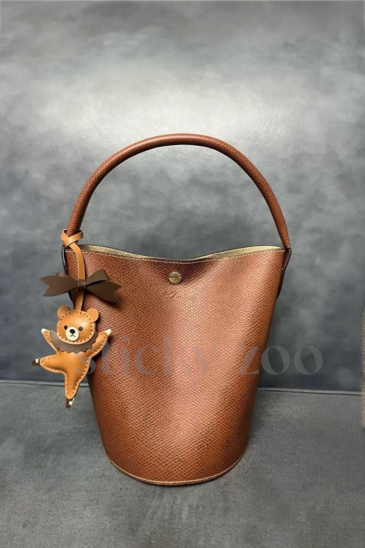 Both editions of the ballet bear charm — leather strap loop for bags, or 18K gold-plated keychain clip.