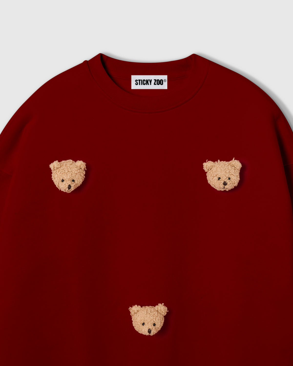 Detail view of scattered plush bear faces on STICKYZOO sweatshirt showing dimensional hand-stitched craft