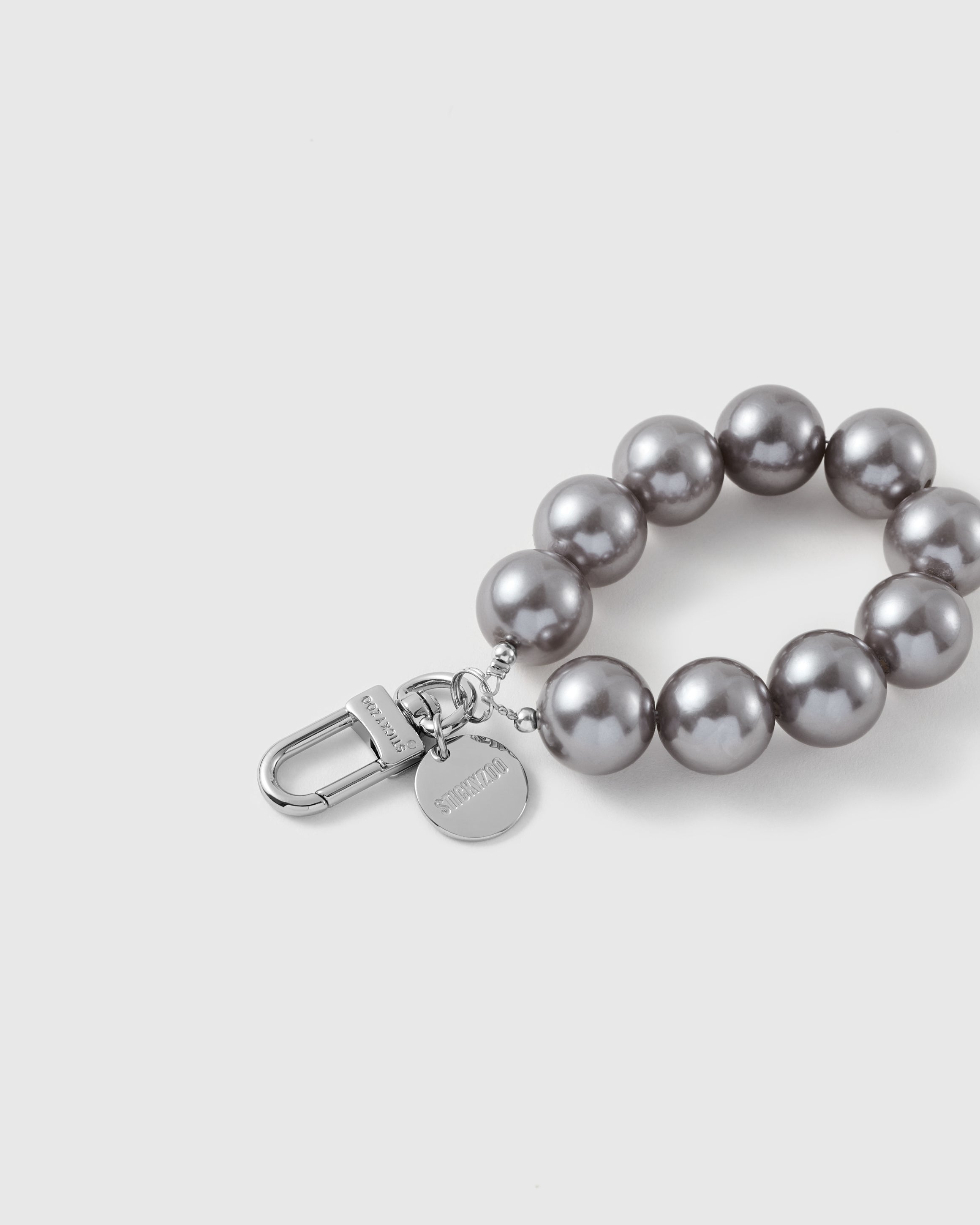Close-up of the silver-tone hook, engraved STICKYZOO disc and grey pearl-style beads — soft even sheen